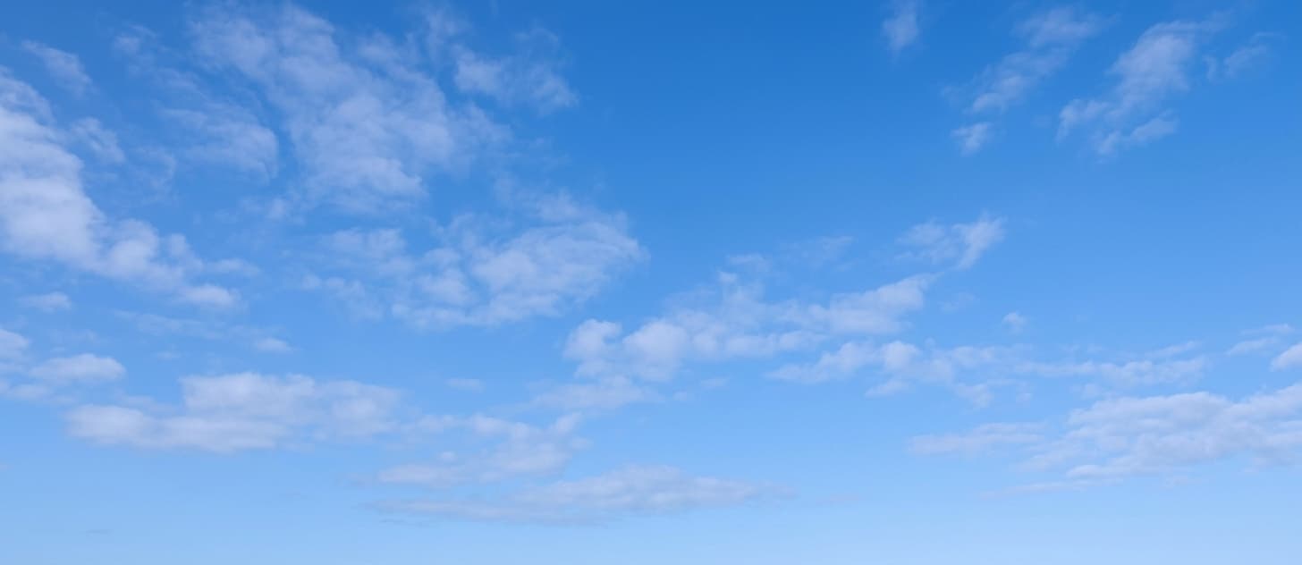 Wide panoramic view of a bright blue sky with scattered, wispy white clouds.